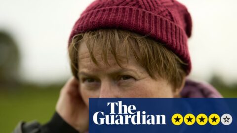 Monica Dolan, as Catherine Corless, touches her ear with a concerned expression outdoors